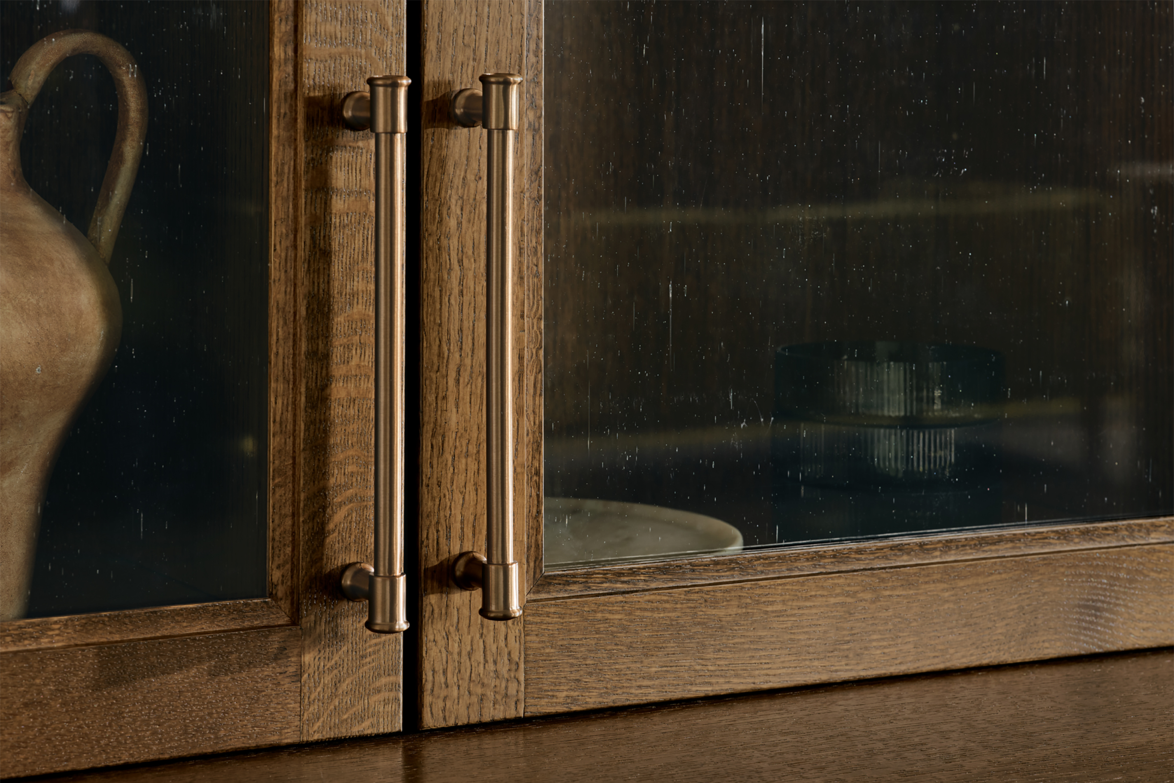 Detail of a dining room hutch featuring KraftMaid Quartersawn Oak door with Antiquity glass insert and brushed bronze hardware